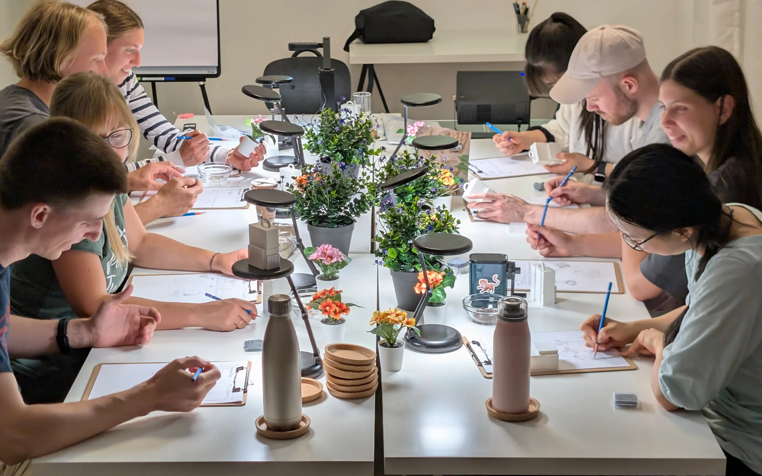 Kursteilnehmer:innen zeichnen gemeinsam an einem langen Tisch im Kursraum