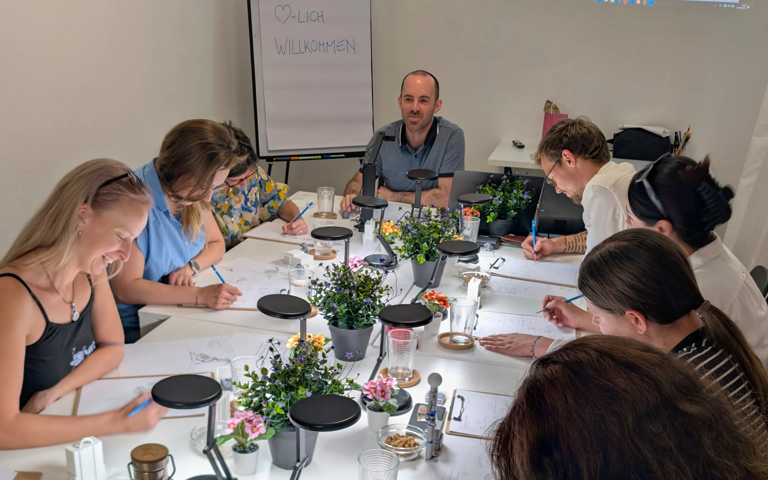 Max Berg sitzt mit einer Kursgruppe beim Zeichnen am langen Tisch